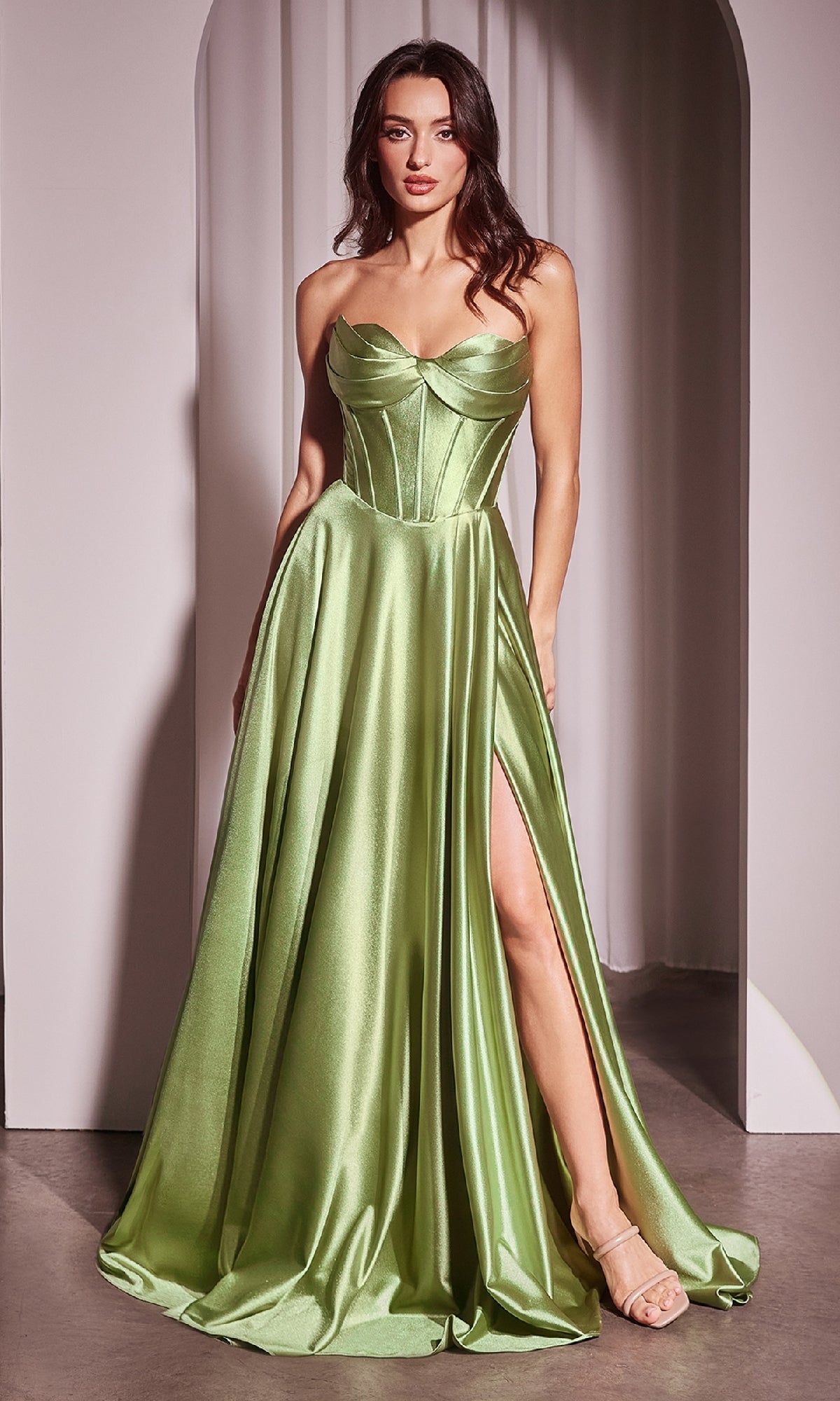 A woman stands in a doorway wearing the Ladivine CD378, a strapless long a-line prom dress with a shiny light green corset-style bodice and high thigh slit, paired with nude heels.